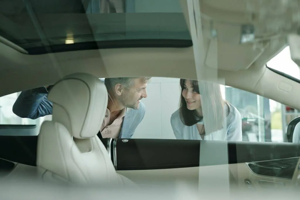 Happy customers standing by car in auto center and bending forwards to window