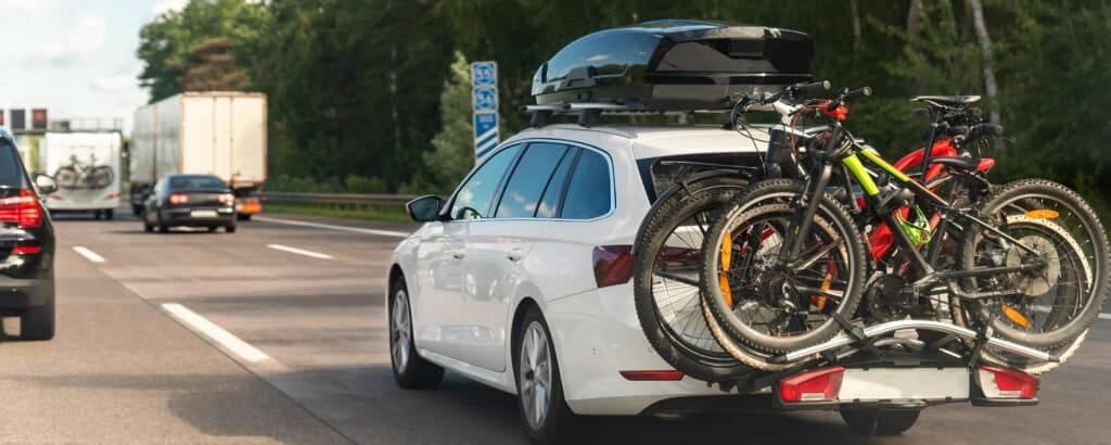Back view modern white family wagon car with mounted roof box trunk and bike tail carrier driving